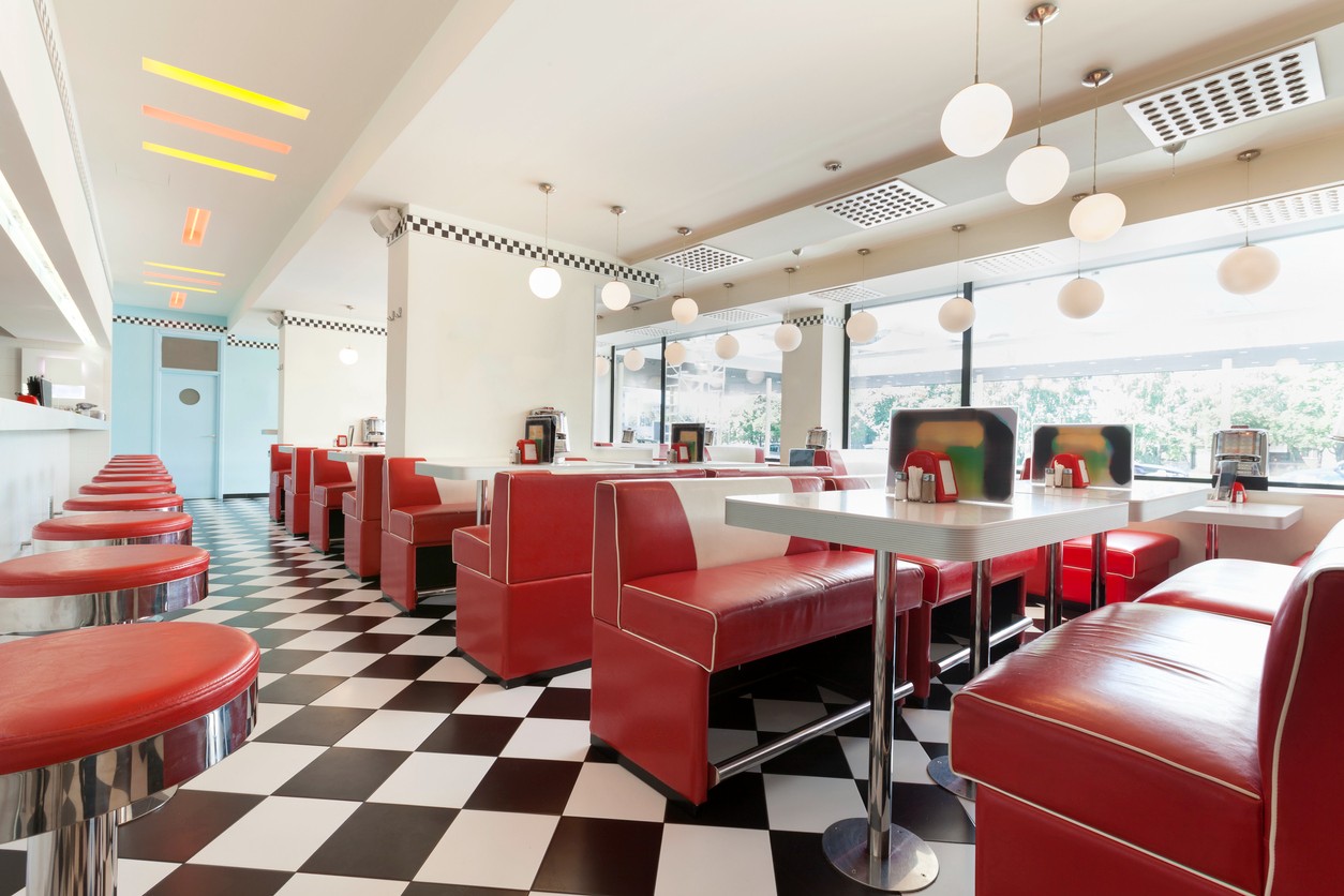 Retro diner restaurant with red vinyl booths, tables and red stools at a long counter bar