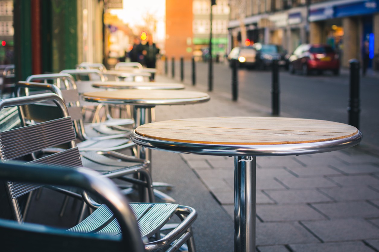 Metal restaurant tables and chairs on an outdoor sidewalk in a city.