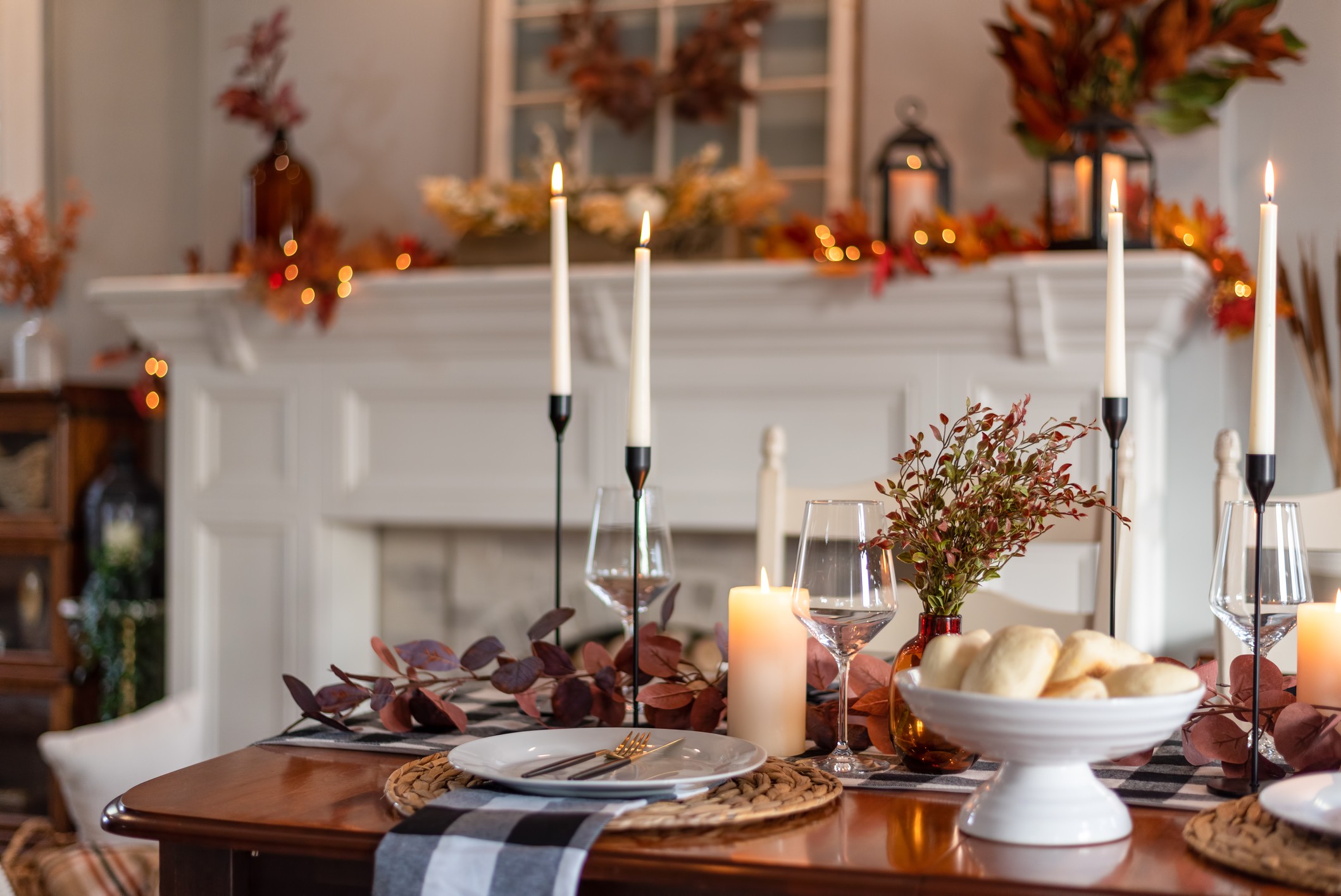 A dining table elegantly set for Thanksgiving dinner with a decorated fireplace in the background.
