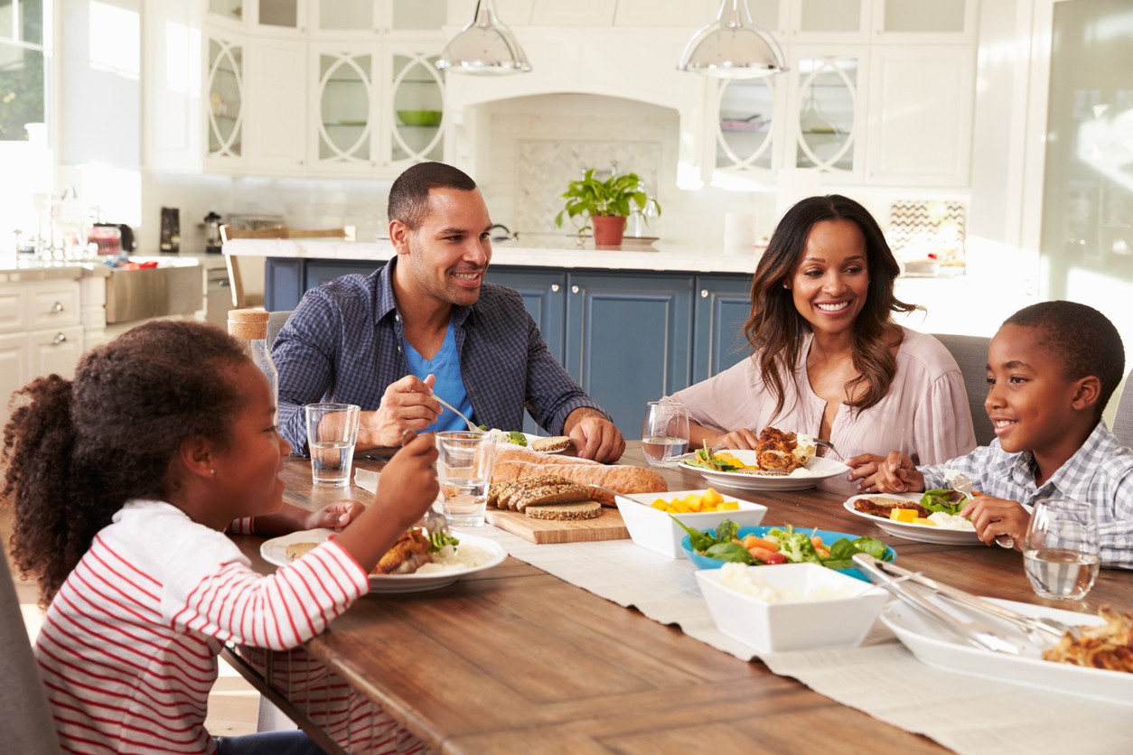 An African-American family eats dinner together at the dining table.