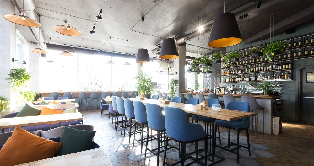 A modern restaurant with upholstered barstools, restaurant booths and tables.