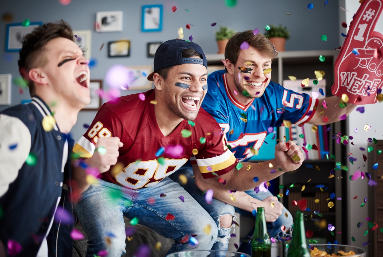 Men cheering and watching football on TV at home.