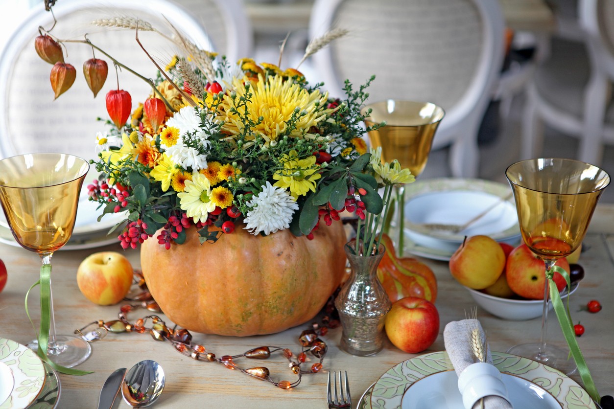 Thanksgiving centerpiece of flowers in a pumpkin surrounded by place settings.