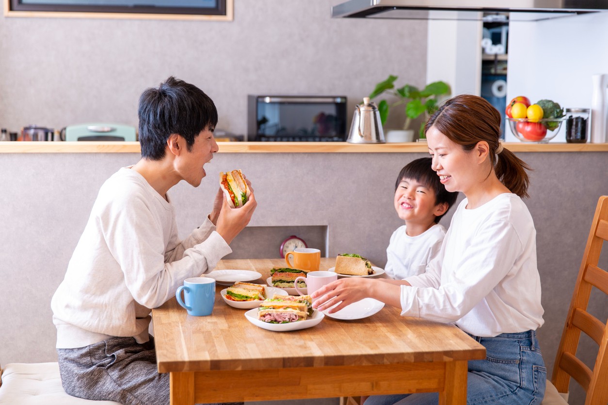 Family eating on a pub table. Mom and dad sitting on table watching dad eat a burger.